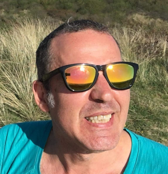Mikel (40-something male, with short, dark hair) wearing the sunglasses with rainbow colored reflection that inspired the logo of the coaching grant bearing his name. 